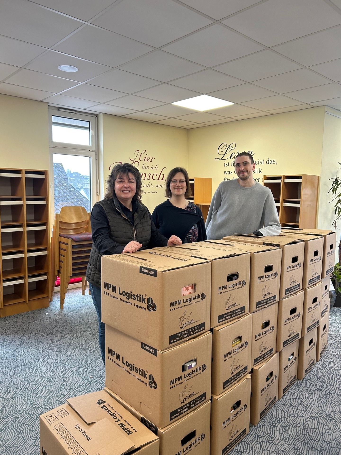Stadtbürgermeisterin Melanie Leicher, Bibliotheksleiterin Carina Senko und Lukas Wilhelmi vom Team der Stadtbibliothek stehen vor gepackten Kisten: Der Umzug der Stadtbibliothek Montabaur ist in vollem Gange.