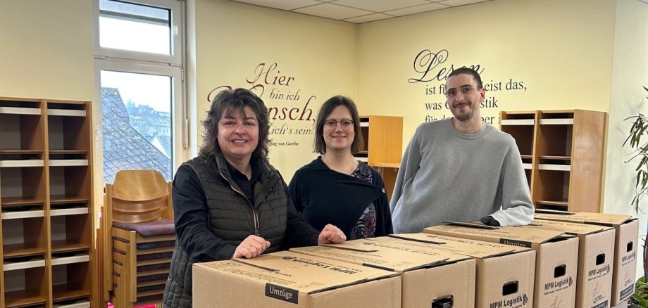 Stadtbürgermeisterin Melanie Leicher, Bibliotheksleiterin Carina Senko und Lukas Wilhelmi vom Team der Stadtbibliothek stehen vor gepackten Kisten: Der Umzug der Stadtbibliothek Montabaur ist in vollem Gange.