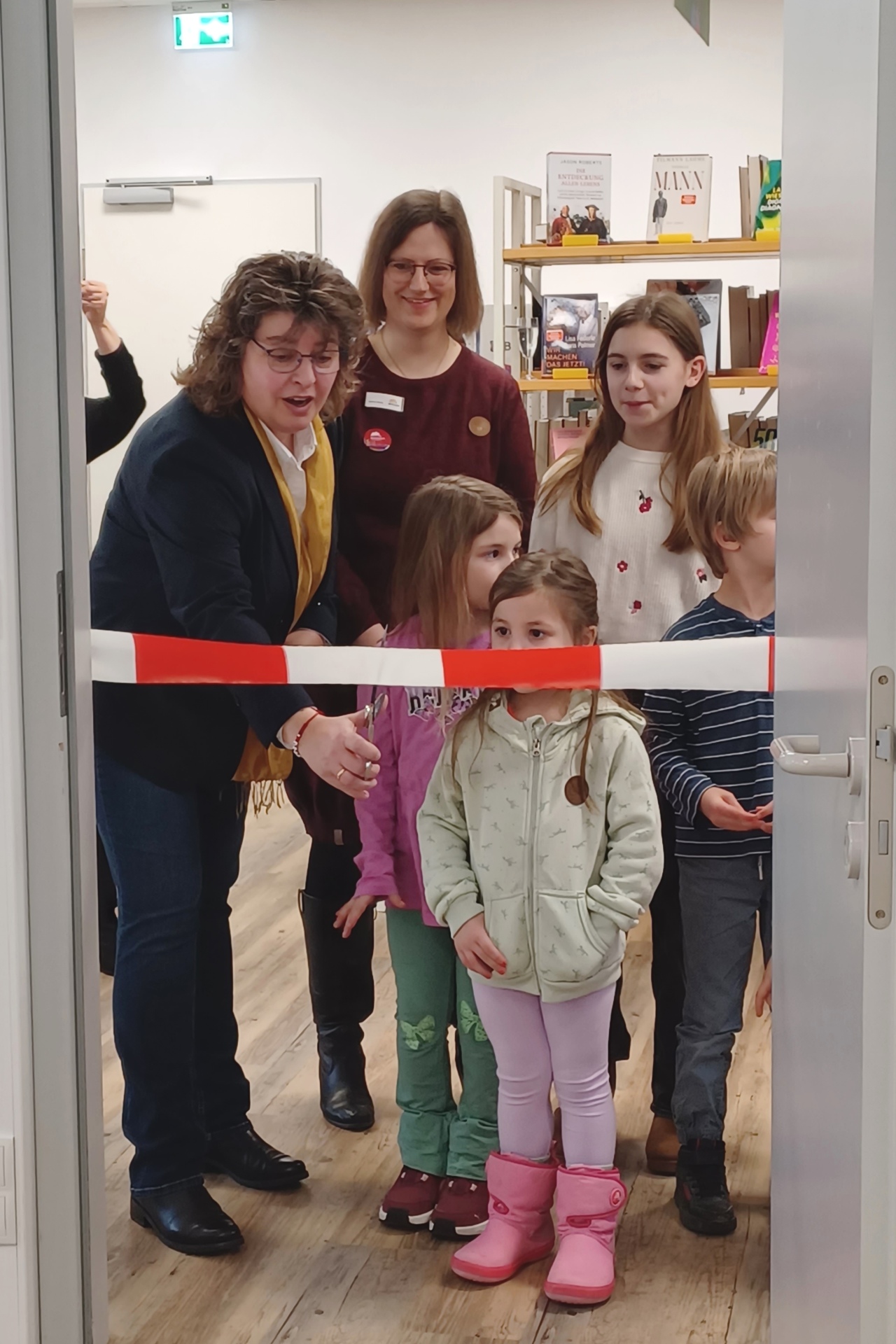 Stadtbürgermeister Melanie Leicher (l.) scneidet das Absperrband durch. Unterstützt wurde sie von Bibliotheksleiterin Carina Senko und vielen neugierigen Kindern.