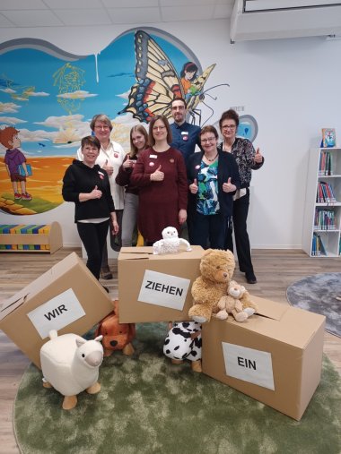 Wir ziehen ein. Stolz präsentiert das Team der Stadtbibliothek mit (v.l.) Diane Müller-Lopez, Susanne Walter-Hahn, Luisa Merz, Carina Senko, Lukas Wilhelmi, Klaudia Zude und Ursula Kingen die leeren Umzugskartons. Im Hintergrund das Wandgemälde von Dater127.