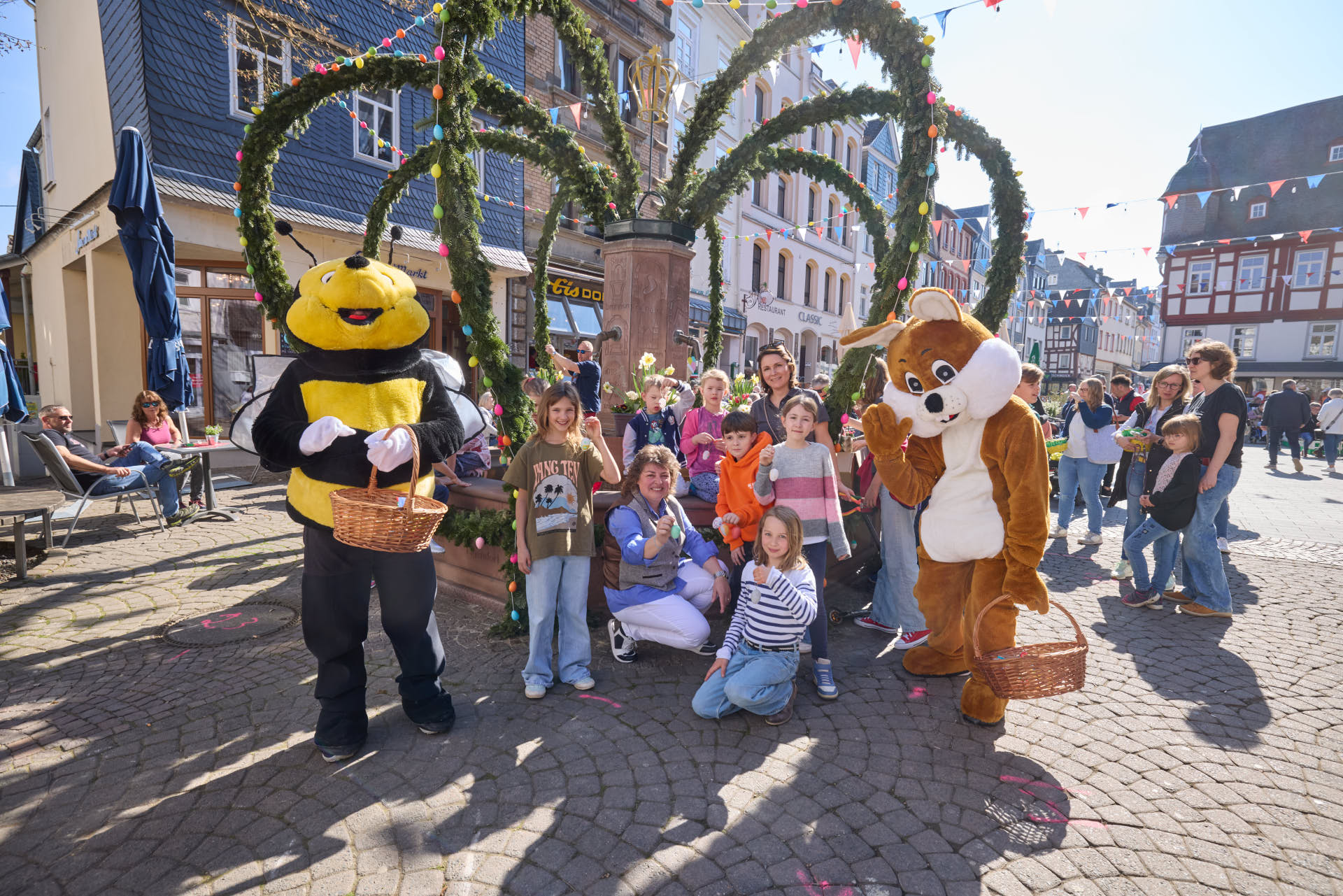 Schüler der Joseph-Kehrein Schule stehen mit Stadtbürgermeisterin Melanie Leicher vor dem geschmückten Osterbrunnen.