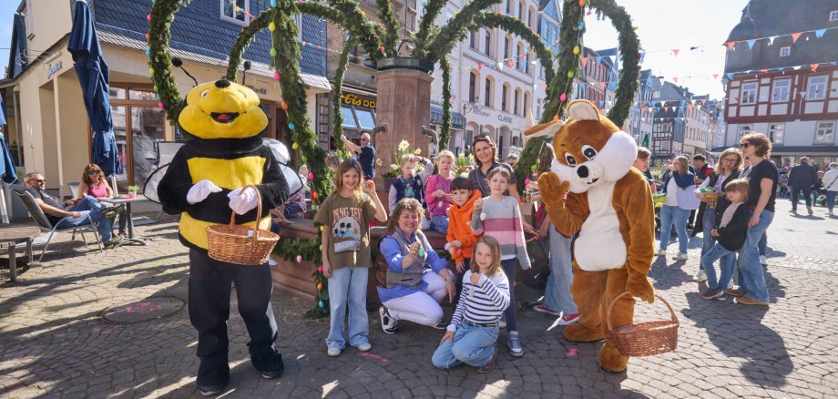 Schüler der Joseph-Kehrein Schule stehen mit Stadtbürgermeisterin Melanie Leicher vor dem geschmückten Osterbrunnen.