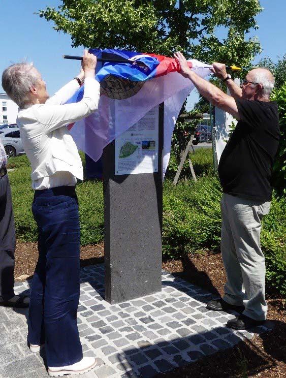 Außenaufnahne von zwei erwachsenen Personen bei der feierlichen Enthüllung einer Info-Stele