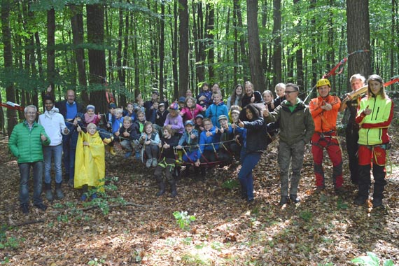 Das Bild zeigt 30 Kinder und einige Erwachsene bei regnerischem Wetter im Wald