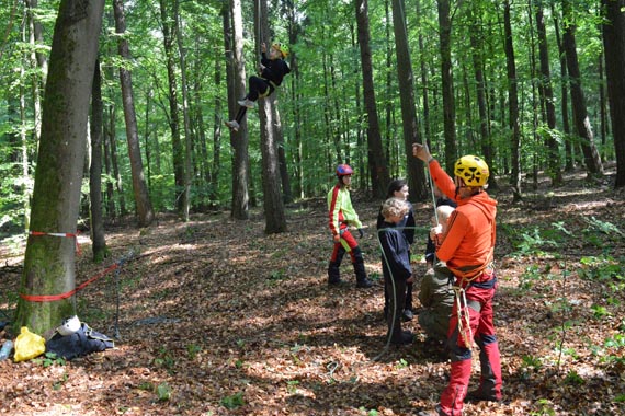 Das Bild zeigt drei Kinder im Wald bei der Vorbereitung zum "Waldklettern"