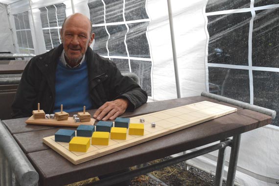 Das Bild zeigt einen erwachsenen Mann, der vor hölzernen, mittelalterlichen Spielen am Tisch sitzt.