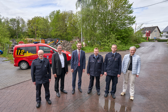 Außenaufnahme von sechs erwachsenen Personen, die vor einem geparkten Feuerwehrfahrzeug stehen