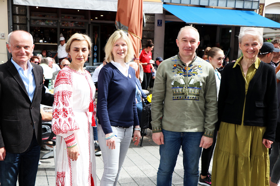 Das Bild zeigt 5 erwachsene Personen sowie Passanten im Hintergrund