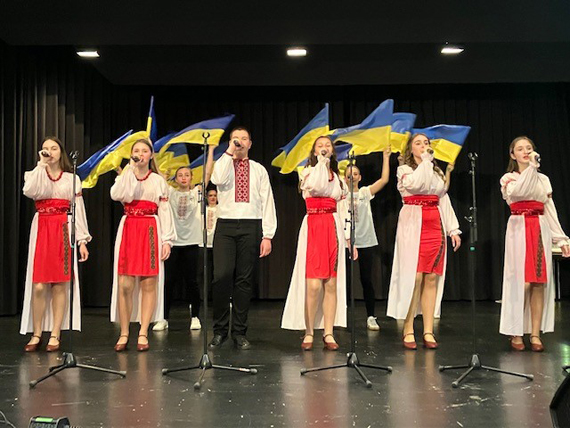Das Bild zeigt einen Folklorechor beim Gesangsauftritt auf einer Bühne 