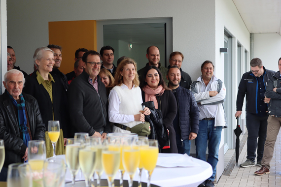 Das Bild zeigt eine große Gruppe von Erwachsenen beim Sektempfang einer Eröffnungsfeier
