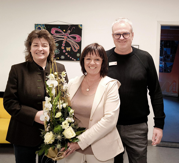 Das Bild zeigt drei Erwachsene bei eines einer Gratulation 