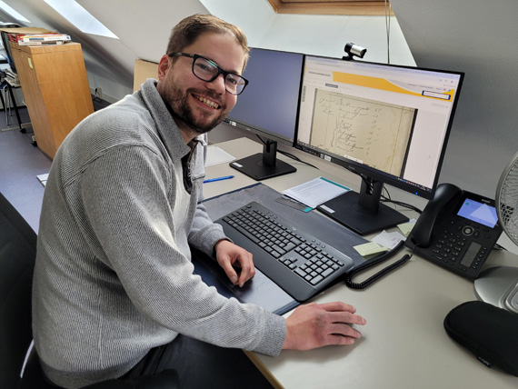 Das Bild zeiigt einen Mann, der am Schreibtisch vor seinem Computerbildschirm sitzt 