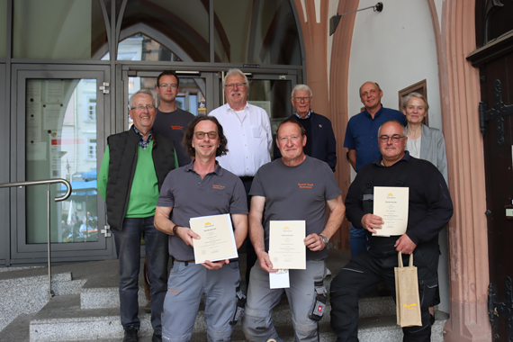 Das Bild zeigt eine Gruppe von 9 Erwachsenen auf den Eingangsstufen des historischen Rathauses, drei davon halten eine Urkunde in den Händen.