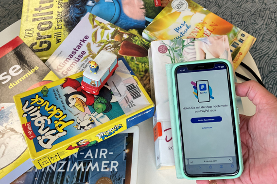 Das Bild zeigt eine ungeordnete Sammlung von Flyern, Spielen und ein Smartphone 